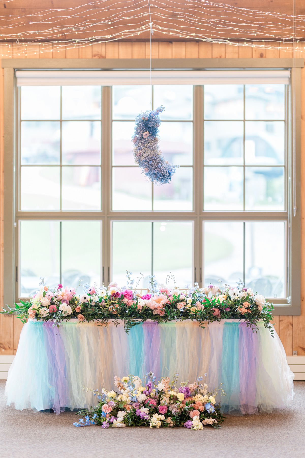 Burlington Vermont wedding florist Taylor Swift Lover album themed wedding. Pastel color palette at Sugarbush Vermont wedding venue reception sweetheart table flowers and a babys breath moon shaped ceiling chandelier floral installation